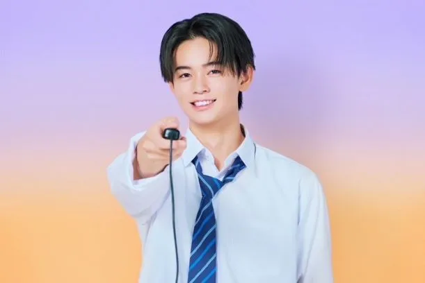 陣野 奏汰のビジュアル。撮影用のリモコンを右手に持っている。黒髪のセンター分け。白シャツにブルーのストライプネクタイをしている。